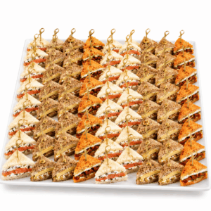 Un plateau blanc sur lequel sont soigneusement disposées des rangées de « PLATEAU DE 80 MINI CLUB SANDWICHS », chaque sandwich triangulaire étant maintenu par un cure-dent décoratif. L'assortiment se compose de différentes variétés de pain et de garnitures bien visibles.