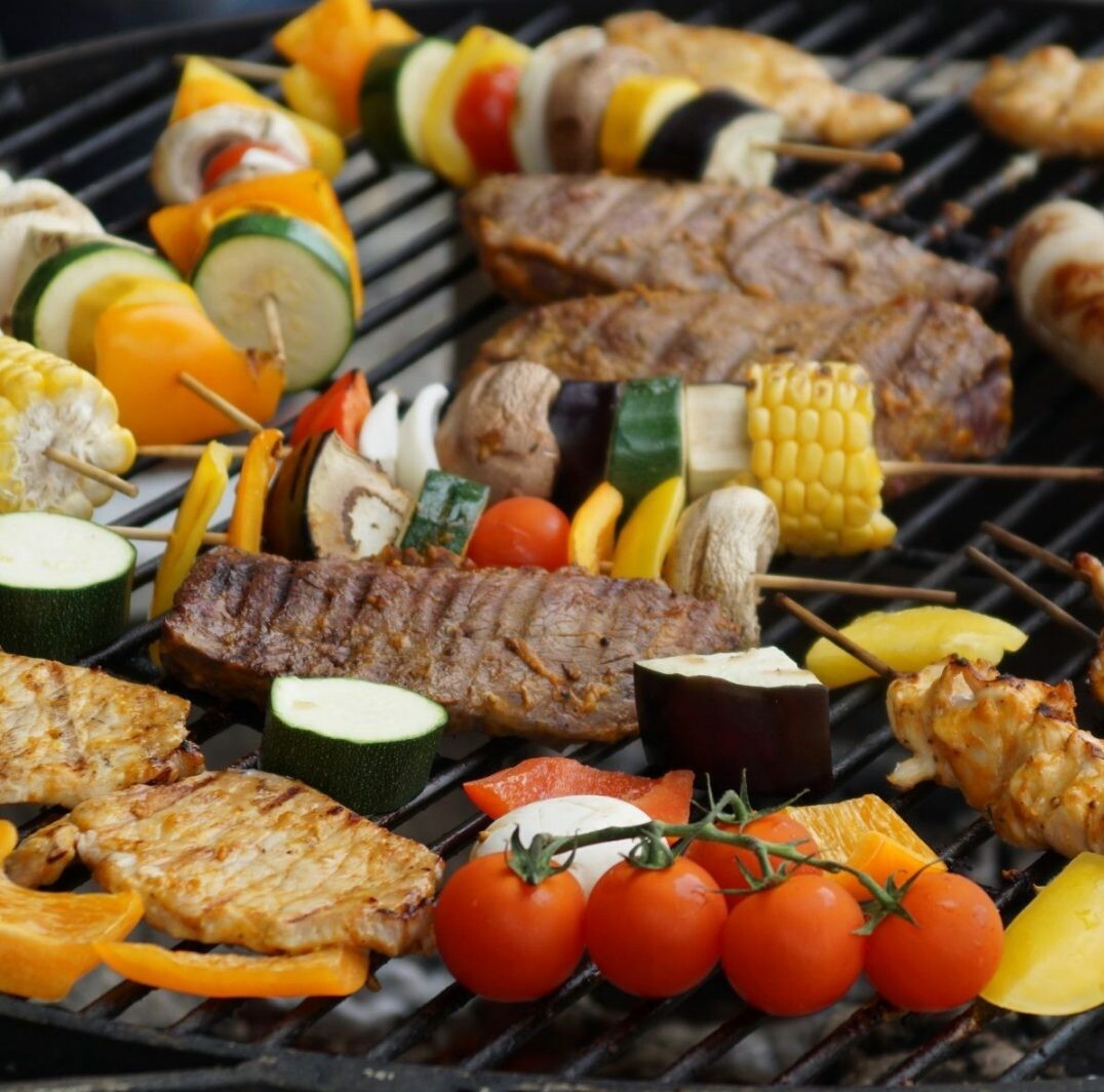 La BROCHETTE VEGETARIENNE BARBECUE présente des légumes colorés, des tomates cerises, du maïs et des brochettes qui cuisent sur le gril - parfait pour les événements barbecue.