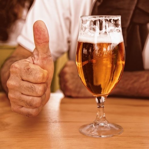Une personne lève le pouce à côté de la TIREUSE À BIÈRES PRO 2 BECS sur une table en bois, montrant ainsi son approbation et son plaisir - comme dans un vrai bar à bières.