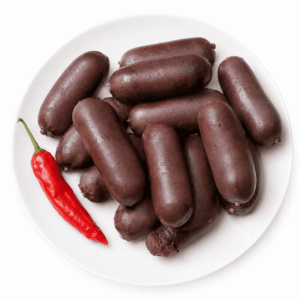 Une assiette blanche sur laquelle sont disposés plusieurs morceaux de BOUDIN ANTILLAIS 80 GR (commande minimum : 6 pièces), un boudin noir, accompagnés d’un piment rouge, le tout sur fond blanc.