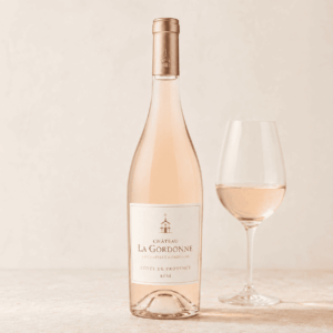 Une bouteille de CHÂTEAU LA GORDONNE LA CHAPELLE GORDONNE ROSÉ 75 cl AOP Côtes de Provence est posée à côté d'un verre à vin rempli, sur une surface claire, devant un fond neutre.