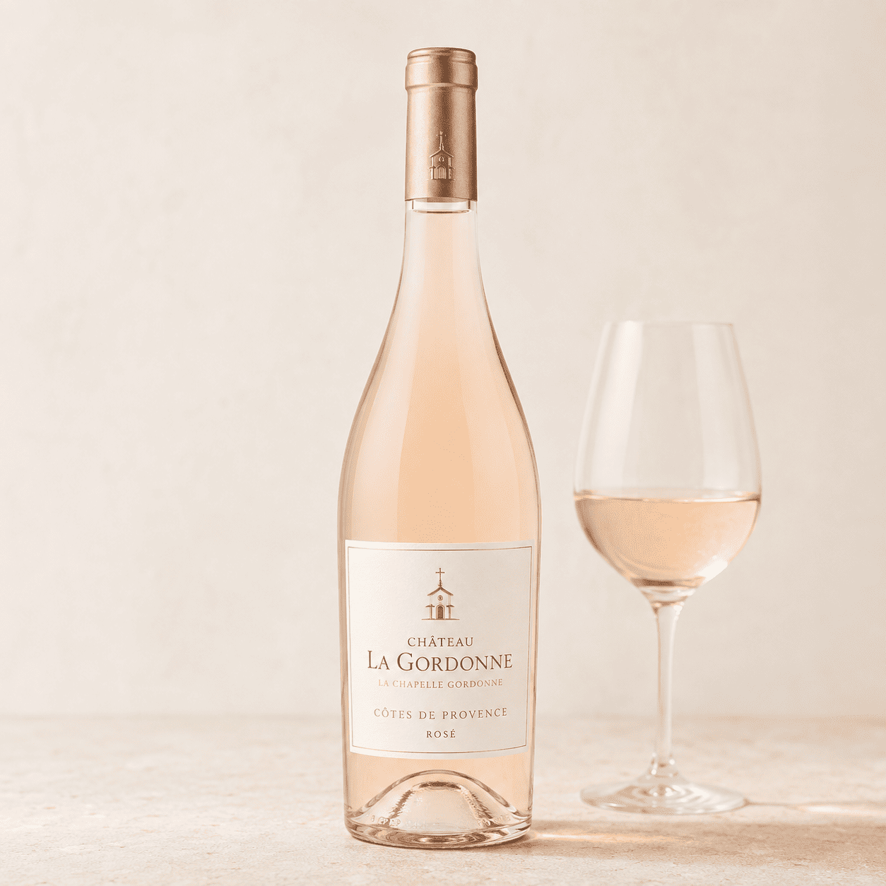 Une bouteille de CHÂTEAU LA GORDONNE LA CHAPELLE GORDONNE ROSÉ 75 cl AOP Côtes de Provence est posée à côté d'un verre à vin rempli, sur une surface claire, devant un fond neutre.