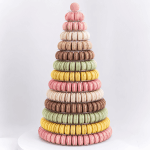 Une grande pièce montée en forme de pyramide composée de 191 macarons, aux couleurs vives (rose, jaune, vert, marron et crème), empilés en anneaux et présentés sur un fond blanc uni.