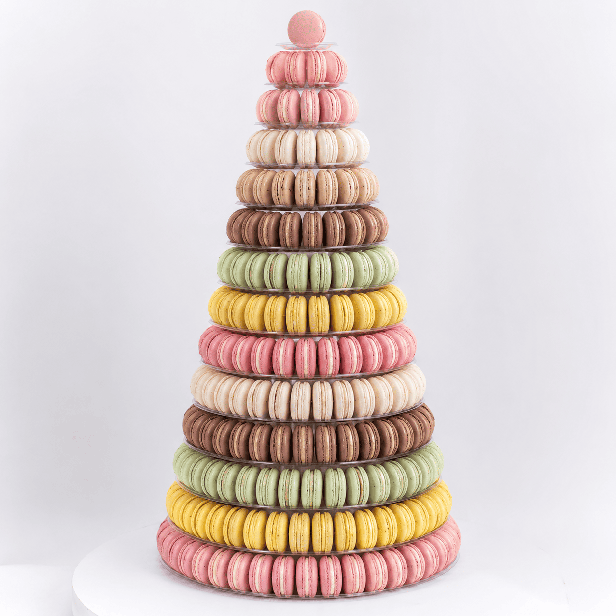 Une grande pièce montée en forme de pyramide composée de 191 macarons, aux couleurs vives (rose, jaune, vert, marron et crème), empilés en anneaux et présentés sur un fond blanc uni.