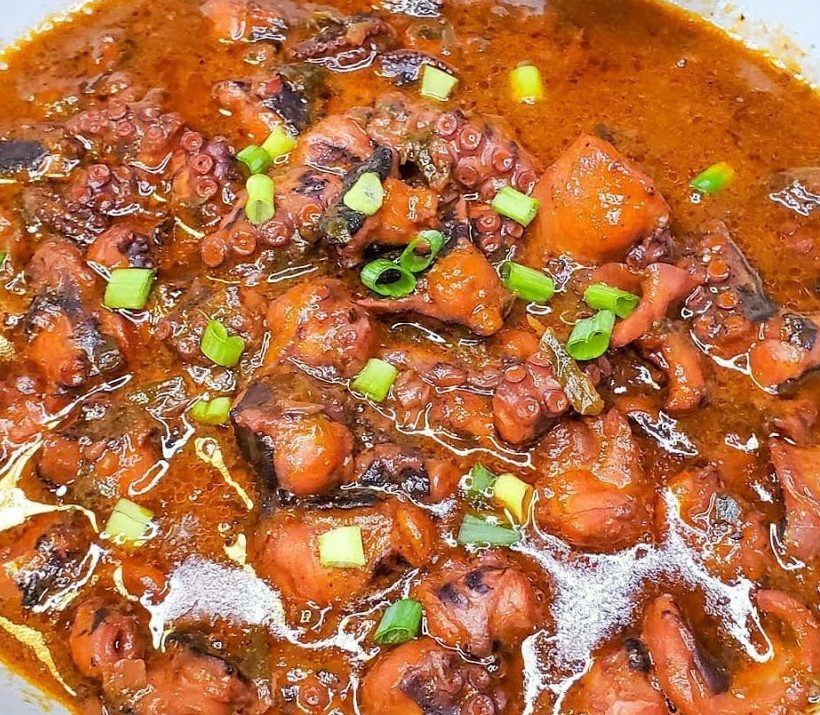 Gros plan sur le FRICASSÉ DE CHATROU (250 g la part), qui présente un poulpe tendre dans une sauce rouge riche, garnie d'oignons verts hachés.
