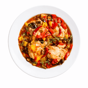Vue de dessus du plat « KEDJÉNOU DE POULET 300 g », composé de morceaux de poulet tendres dans une sauce à la tomate, accompagnés de poivrons rouges et jaunes, d'aubergines et d'herbes fraîches.