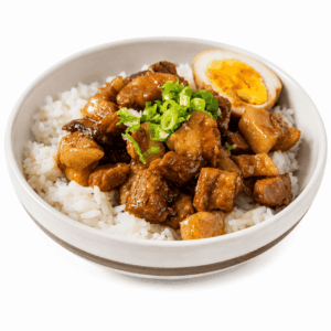 COLOMBO DE PORC (Commande minimum : 5 portions - 300 g par portion) : Un bol de riz blanc garni de porc braisé à la façon Colombo, d’oignons verts hachés et d’un demi-œuf mollet, servi dans un bol blanc sur fond blanc.