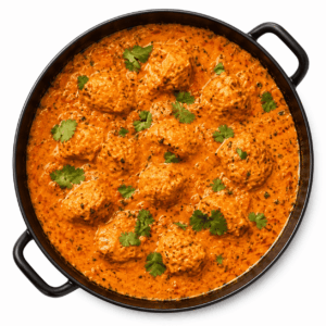 Vue du dessus d'un plat rond noir contenant du CURRY D’AGNEAU 300 g (commande minimum : 5 portions), composé de tendres boulettes d’agneau dans une sauce crémeuse au curry et à l’orange, et garni de feuilles de coriandre fraîche.