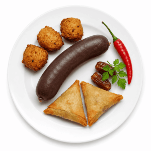 Sur un fond blanc, le « PETIT ASSORTIMENT D’ENTRÉES ANTILLAISES » est soigneusement disposé sur une assiette blanche : une saucisse foncée, trois boulettes frites, deux pâtisseries triangulaires, deux dattes, un brin de coriandre et un piment rouge.