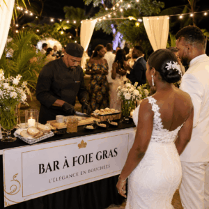 Lors d'une réception de mariage nocturne éclairée par des guirlandes lumineuses, les mariés, vêtus de blanc, regardent un chef préparer des mets à la table en plein air de l'ANIMATION BAR À FOIE GRAS, entourés de leurs invités.