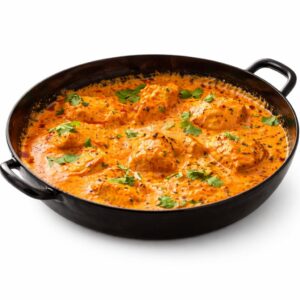 Une casserole noire de CURRY D'AGNEAU crémeux et orangé, garnie de coriandre fraîche et contenant plusieurs koftas ronds, sur fond blanc. Commande minimale : 5 pièces (300g par pièce).