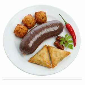 Une assiette blanche sur laquelle est disposé avec soin le « PETIT ASSORTIMENT D’ENTRÉES ANTILLAISES », composé d’un boudin noir, de trois beignets, de deux samosas, d’un piment rouge, de deux dattes et d’un brin de persil.
