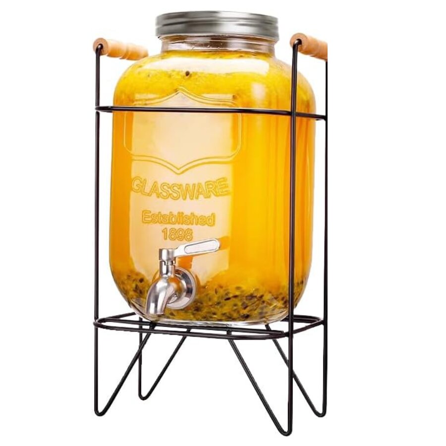 Un distributeur de boisson en verre « PLANTEUR FAIT MAISON » (4 litres), muni d’un robinet en métal et rempli d’un liquide jaune et de morceaux de fruits, repose sur un support en fil de fer noir doté de poignées en bois. Le bocal est muni d’un couvercle métallique à visser.