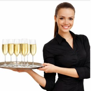 Une femme souriante, vêtue de noir, représentant le PERSONNEL DE SERVICE (Formule 4h), tient un plateau sur lequel sont posés six verres à champagne remplis, photographiée en plan isolé sur fond blanc.