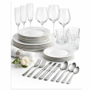 Un service de table raffiné de la collection « TOUT L’ART DE LA TABLE », composé d’assiettes blanches, de bols, de verres, de verres à vin, de couverts et d’une serviette ornée d’une rose blanche et de gypsophile, le tout disposé avec élégance sur un fond d’un blanc immaculé.