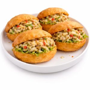 Sept sandwichs ronds MINI BOKIT GARNI MORUE (80g chacun), fourrés d'un savoureux mélange de morue et de légumes, servis sur un pain doré, légèrement croustillant et aux herbes, présentés sur une assiette blanche. Minimum 7 pièces par commande.