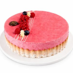 La CHARLOTTE(S) AUX FRUITS ROUGES est un gâteau rond à base de mousse rose et de génoise légère, garni de baies fraîches, de décorations en chocolat blanc et d'un disque en chocolat, servi sur une assiette blanche.