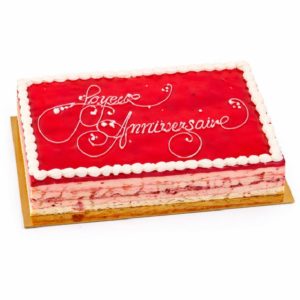 Le gâteau FRAMBOISINE(S) présente une forme rectangulaire avec un dessus rouge brillant, un bord de glaçage blanc et "Joyeux Anniversaire" en écriture blanche, présenté sur une planche dorée. Choisissez le nombre de portions que vous souhaitez.