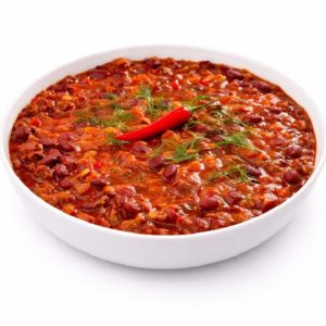 Un bol blanc rempli de chili con carne comprenant des HARICOTS ROUGES, de la viande hachée et une riche sauce tomate, garni d'aneth frais et d'un piment rouge entier. Commande minimum : 5 portions (250g chacune).