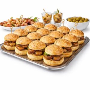 Un plateau métallique présente des MINI-BURGERS AU FOIE GRAS (commande minimum de 20 pièces, 25g/pc), chaque burger étant accompagné d'un petit pain aux graines de sésame et d'une brochette. À l'arrière-plan, des bols d'olives, des amuse-gueule et des desserts en couches.