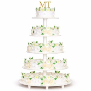 Le PIÉCE MONTÉE BELLA ROSA 50 PARTS est un gâteau blanc à six étages orné de roses blanches, de marguerites, de feuilles vertes sur chaque étage, et terminé par les initiales dorées MT, présenté sur un support à étages blanc.