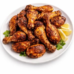 Une assiette blanche contient des PILONS DE POULET A ROTIR 85 GR (Minimum commande 10 pilons), des pilons de poulet assaisonnés et rôtis, garnis de persil et de quartiers de citron.