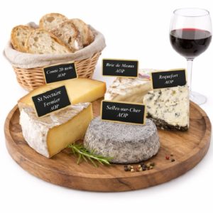 PLATEAU DE FROMAGE : Un plateau en bois avec cinq fromages français étiquetés - comté, brie de Meaux, roquefort, saint-nectaire et Selles-sur-Cher - servi avec un verre de vin rouge et une corbeille de pain tranché en arrière-plan.