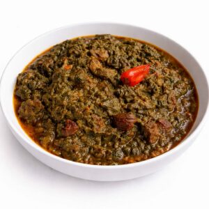 SAKA SAKA (300 g) : Un bol blanc contient un épais ragoût vert foncé et brun surmonté d'un piment rouge entier, mettant en valeur de copieux morceaux de viande et de légumes.